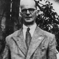 Upper torso of balding, bespectacled man wearing suit with tie.