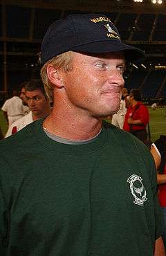 Candid chest-up photograph of Gruden on a football field wearing a green t-shirt and a black baseball cap