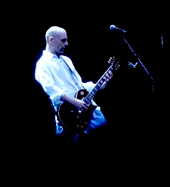 A man in a white shirt playing guitar on stage