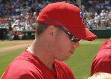 A brown-haired man wearing a red baseball cap with a blue p on it