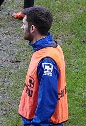 White man with dark hair and beard, wearing sports kit outdoors