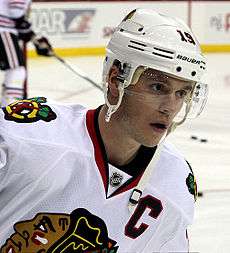 Jonathan Toews in a white away Blackhawks jersey and wearing a white helmet with a clear shield covering his eyes.