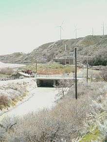 A narrow canyon with a river flowing through it. Railroad tracks are on the left side of the river. A building is on the right side.