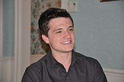 Hutcherson with slicked-back hair, wearing a black button-up dress shirt