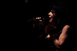 A dark photograph of a woman singing into a microphone