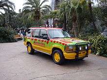 A utility car painted in green, yellow and red colors in a jungle park environment.