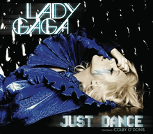 Lady Gaga laying down wearing a dark blue dress with a big, layered collar. Her right hand touches her forehead. Beneath her left eye is a blue-colored lightning-shaped sticker.