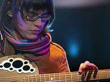 A bespectacled woman plays a guitar.