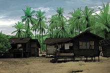 Two wooden floures on stilts stand in front of tall coconut trees.