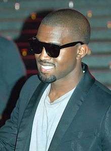 A man dressed in a white shirt and black suit wearing sunglasses.