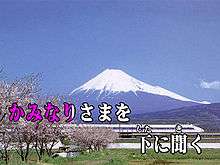 Over a background image of Mount Fuji and a Shinkansen train two lines of Japanese text. The first half of the first line is colored red-violet, the rest white. The text reads "かみなりさまを　下 に聞く".