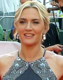 Kate Winslet facing the camera with blonde hair and a grey dress on