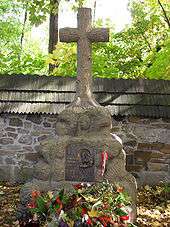 A stone cross atop a large rock. A plaque mounted on the rock reads: "Ostaszkow, Starobielsk, Kozielsk, Katyń 1940", followed by "Zwiazek Sybrakow".
