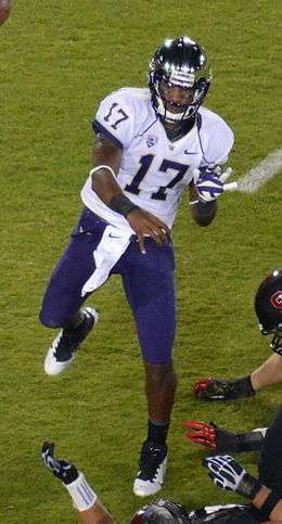 An African-American man wearing a white football jersey emblazoned with number 17 and purple pants throws a pass; the hands of various defenders are visible.
