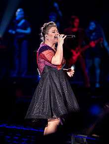An image of Clarkson, wearing a sequined fuchsia and black dress against a dark background.