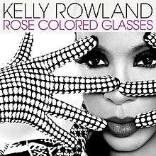 A woman stands with only her face visible. She is wearing polka-dot gloves on her hands which she is holding in front of her face in a spread fashion. The image is black and white. In the foreground at the top, in black text, it reads the artist's name (Kelly Rowland). Directly beneath this it reads the name of the song, in pink text, "Rose Colored Glasses".