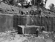 Workers standing in a quarry with a large stone block.