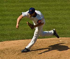 A man sporting a goatee and wearing a dark blue baseball cap with "C" in the middle, a pinstriped jersey and black Nike cleats delivers a pitch.