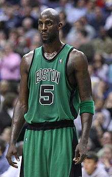 A man, wearing a green jersey with a word "BOSTON" and the number "5" written in the front, is standing in front of the crowd.