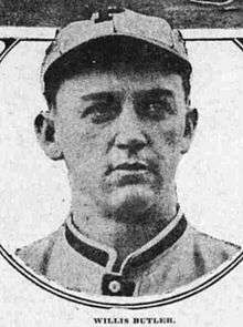 A man in a light-colored baseball uniform and a cap with a "P" on the front looks to the right.