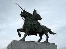 A bronze statue of a knight in armor on a riding horse against gloomy skies