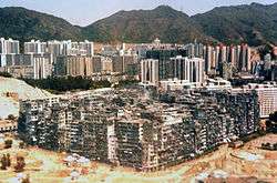 A large solid block of ramshackle buildings varying in height, with many taller buildings and some mountains in the background.