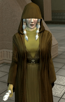 An elderly woman, Kreia, stands, wearing earth-tone robes. The top half of her face, along with her eyes, are covered by dark brown hood, part of another robe worn over her clothes. A braid of hair comes down from each side of her face, and her left hand is missing.