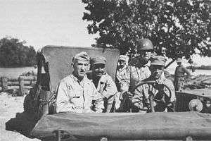 Four officers in a jeep, with a steel helmeted driver. The one on the left is wearing a garrison cap with three stars, the one in the centre a cloth peaked cap with one star, while the one on the right had a steel helmet with two stars.