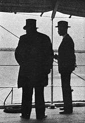 Kruger viewed in silhouette from behind, Bredell to his right. Kruger is wearing his trademark top hat.