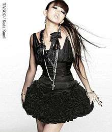 A woman, dressed in a black dress with black-coloured accessories, posing towards the camera with blonde streaks in her hair. The text "Koda Kumi", and "Taboo" are placed on the upper-left side of the image.