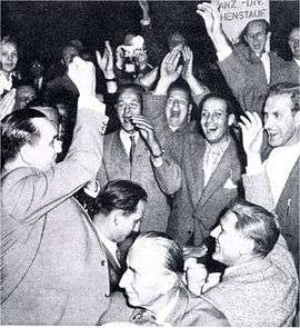 Jubilant crowd at a HIAG convention. Kurt Meyer standing with his fist in the air, while Paul Hausser looks on