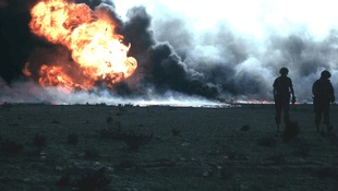 Huge oil fire, with two soldiers in foreground
