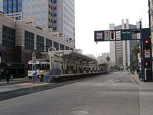 A train station in the middle of a street. A light rail train is stopped on the far track.