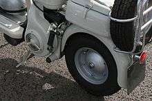 The image shows the port side (left side when facing forward) of a Lambretta Model C. The wheel and the lug nut are visible but there is no visible connection between the wheel and the rest of the scooter.