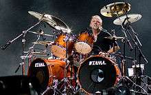 short haired man in a black shirt on a drum kit