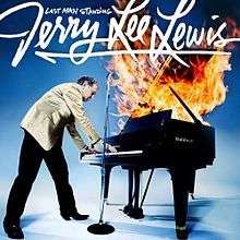 Lewis standing over a piano engulfed in flame with the name of the artist and album in white script above