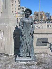 Phot of a statue of a woman in a long dress and a bonnet.
