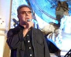 A man wearing a black shirt and glasses is holding a microphone
