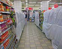 A narrow supermarket aisle, under strip fluorescent lighting, with sections blocked off by white plastic sheeting