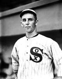 A man in a white baseball uniform with dark pinstripes with "SOX" written on the chest and a baseball cap.