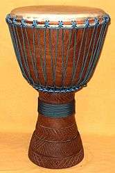 Brown goblet-shaped wood and leather drum with blue rope on an alabaster background