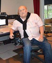 A man wearing a black scarf is sitting in a recording studio.