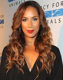 A woman with long, curly brown hair wearing looking directly forward, wearing a black outfit, and red lipstick.
