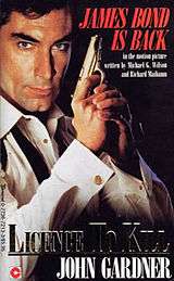 A book cover showing a man holding a pistol. He is wearing a white dress shirt with untied bow tie. The words "JAMES BOND IS BACK" are in the top right hand corner. In the bottom right hand corner are the words "LICENCE TO KILL JOHN GARDNER".