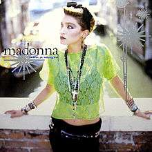 Madonna standing on a bridge wearing a light green see-through top and black pant.