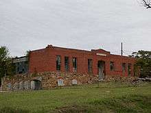 A red brick building with broken windows and lots of vegetation.