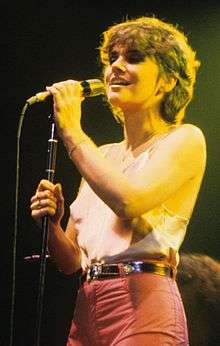 A woman wearing a white sleeveless shirt and pink pants is singing.