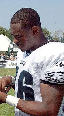 Color photograph of Lito Sheppard, young African-American man, dressed in uniform of Philadelphia Eagles, signing an autograph.