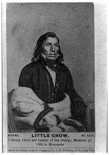 A photograph of a Native American man seated, wearing a suit
