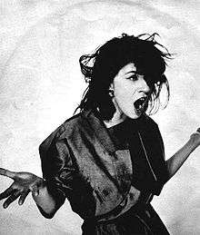 A black-and-white image of a woman with raised hands against a white backdrop.